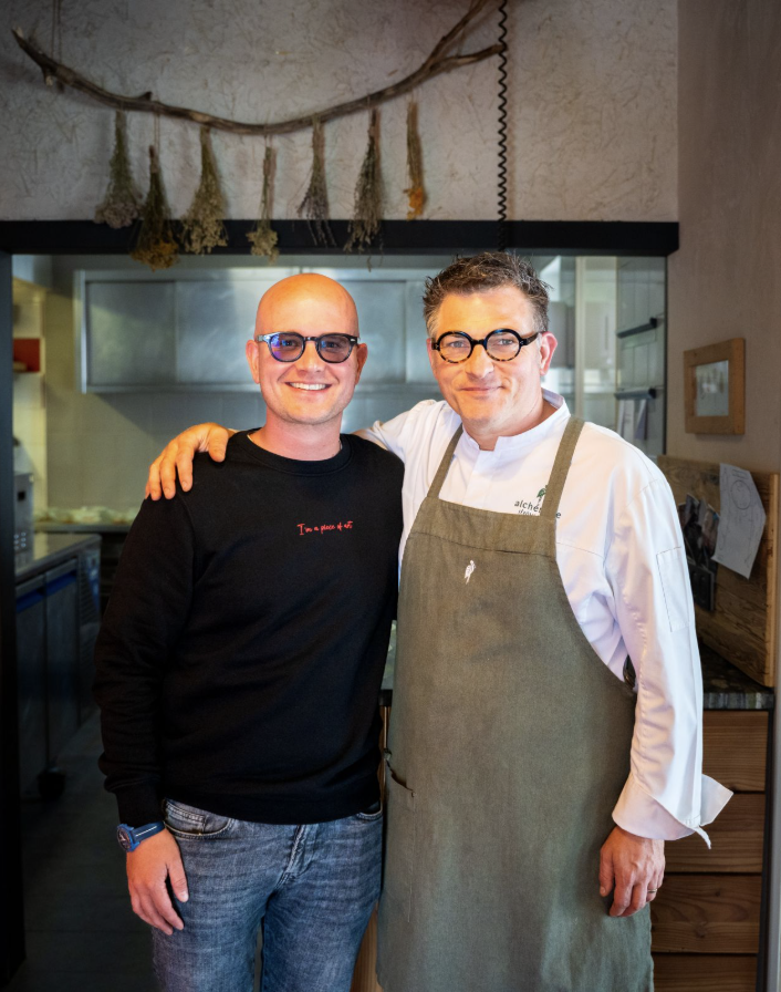 Gründer Ernst Behrens und Koch stehen lächelnd Arm in Arm in einem Restaurantbereich.