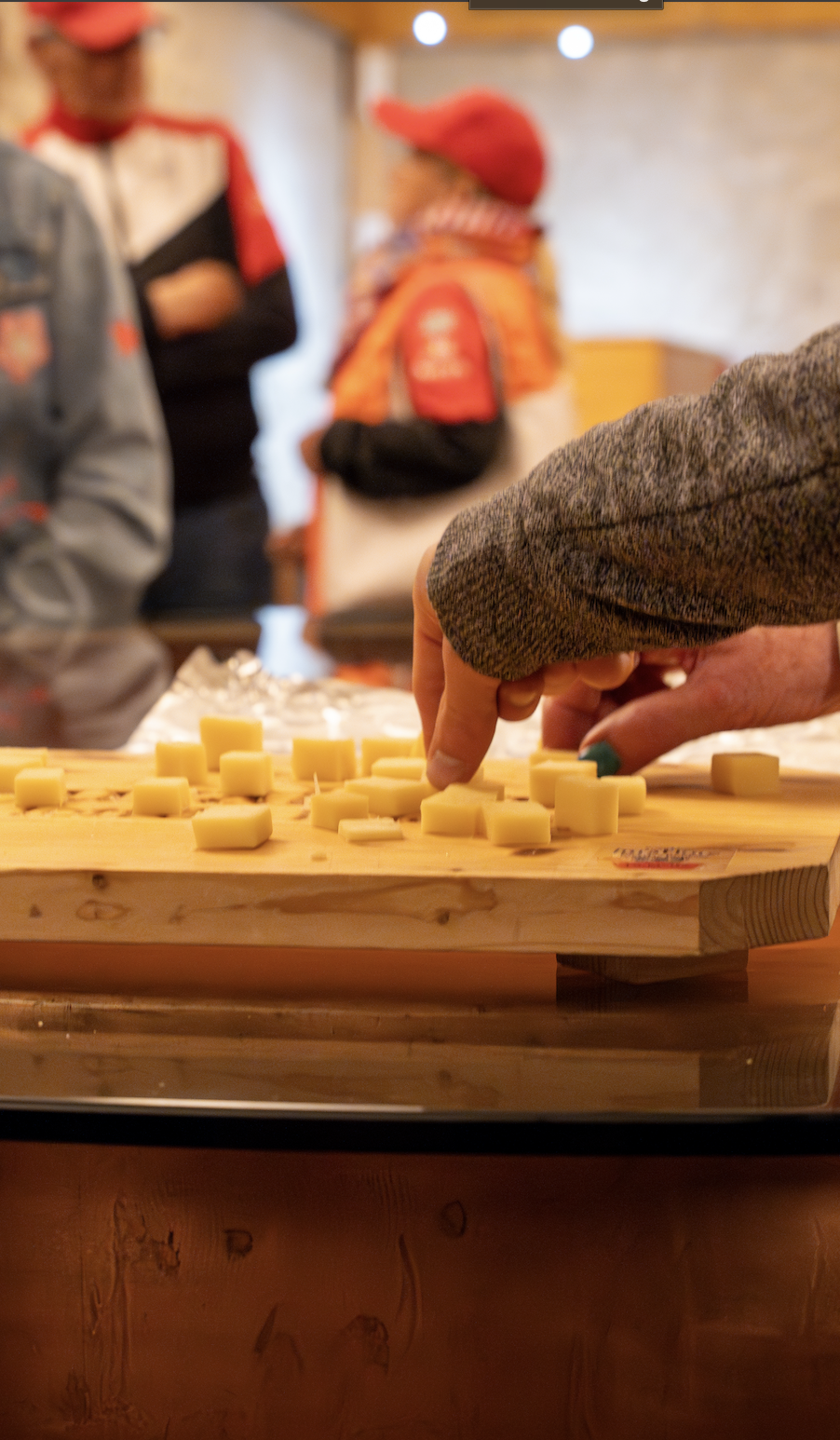 Eine Hand wählt Käsewürfel auf einem Holzbrett bei einer Verkostung aus.